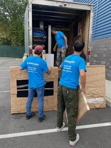 Three Planetary Movers crew members loading wrapped furniture into a box truck